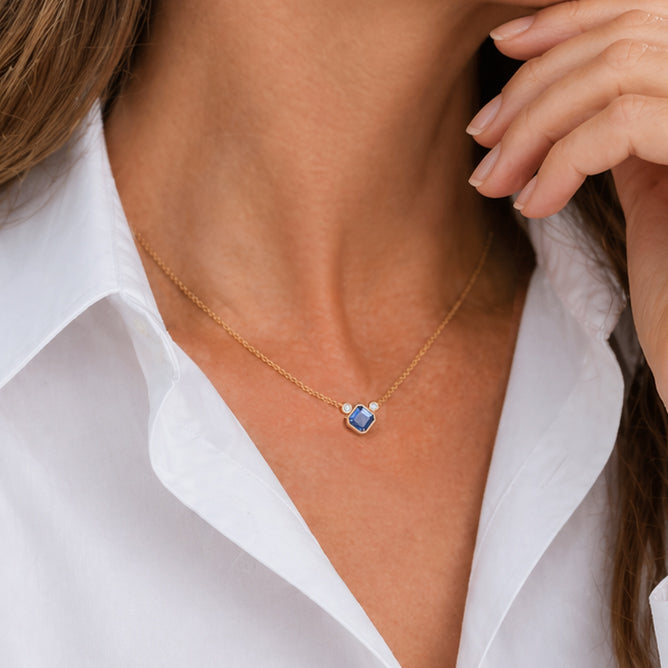 Closeup of a woman wearing layering necklace with Asscher cut Ceylon sapphire and two white diamonds. Plan serré d'une femme portant un collier à saphir et à diamants. Montréal, Canada.